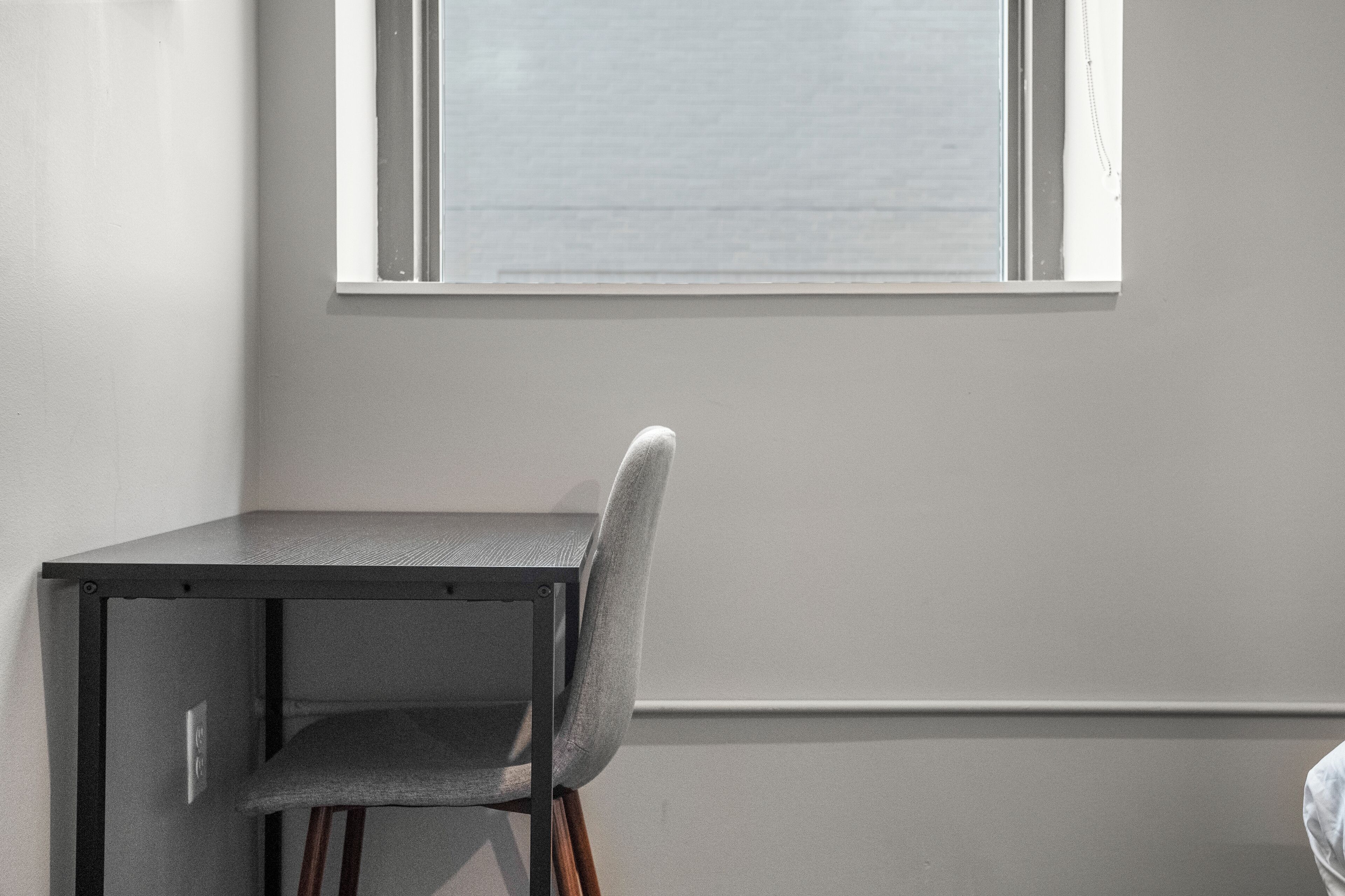 A corner of a room with a table and a chair, a window, and a plain wall.