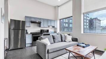 A modern kitchen with grey cabinets, a stainless steel refrigerator, and a grey sofa.