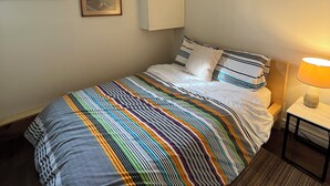 A neatly made bed with striped bedding, a bedside lamp, a framed picture on the wall, and a window with blinds. - 5 min to the beach! Sun filled cottage in Turkey Point (Vittoria)