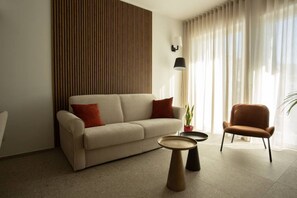 Ein modernes Wohnzimmer mit einer Couch, einem runden Couchtisch, einem Sessel und einer Topfpflanze.