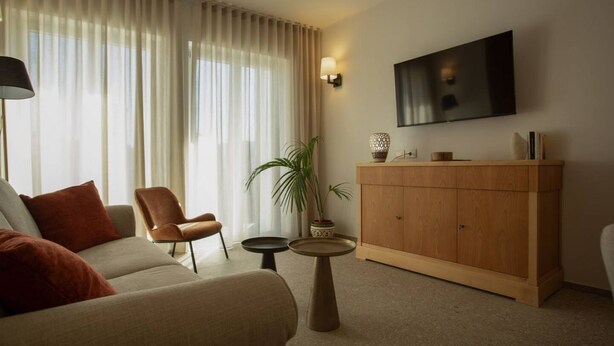 A living room with a sofa, a chair, a small round table, a cabinet, and a TV mounted on the wall. - Palazzo Indaco - RESIDENZA DIAMANTE (Castel di Sangro)