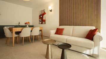 Un soggiorno moderno con divano, due tavolini, zona pranzo con sedie, bancone cucina e un lampadario a parete.