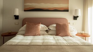 A neatly made bed with a striped bedspread and two pillows, a wall-mounted painting, and two bedside lamps on either side. - Palazzo Indaco - RESIDENZA PERLA (Castel di Sangro)
