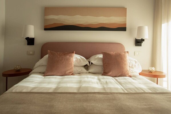 A neatly made bed with a striped bedspread and two pillows, a wall-mounted painting, and two bedside lamps on either side.