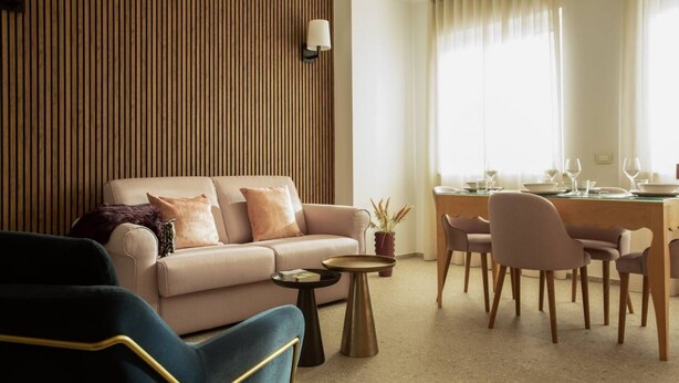 A modern living room with a sofa, chairs, a coffee table, and a dining area with a table set for a meal. - Palazzo Indaco - RESIDENZA PERLA (Castel di Sangro)
