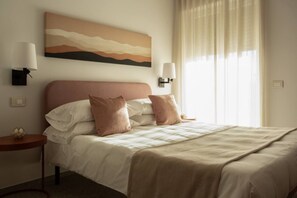 Une chambre d’hôtel avec un grand lit, deux lampes de chevet, un tableau au mur et une fenêtre avec des rideaux.