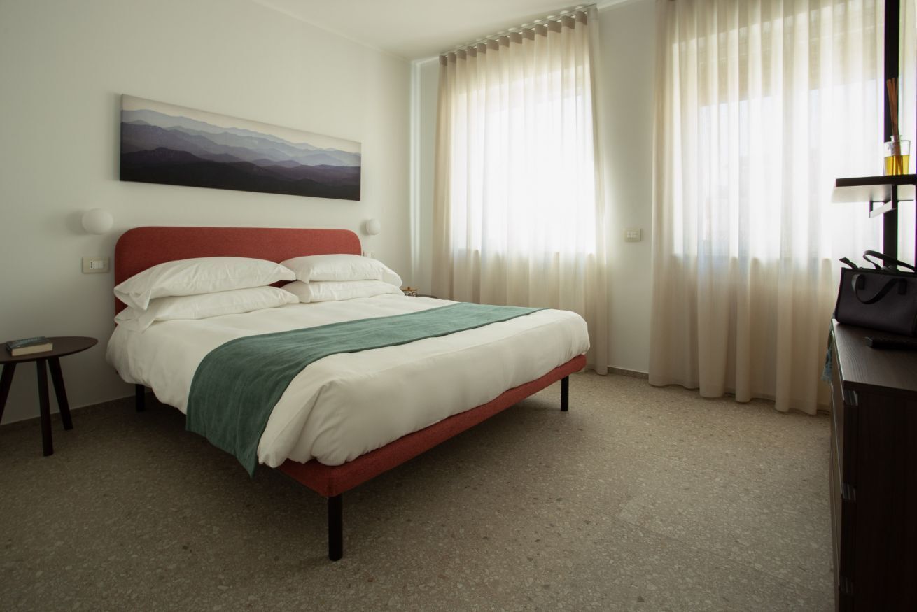A neatly made bed with a red headboard, a bedside table with a book, and a painting on the wall.