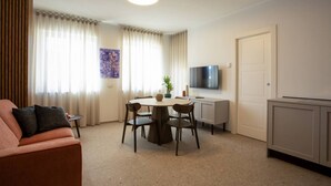 A modern living room with a round dining table, a sofa, a TV, and a door. - Palazzo Indaco - RESIDENZA RUBINO (Castel di Sangro)