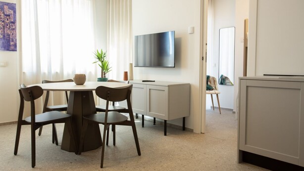 A modern dining area with a round table, four chairs, a potted plant, and a flat-screen TV mounted on the wall. - Palazzo Indaco - RESIDENZA RUBINO (Castel di Sangro)
