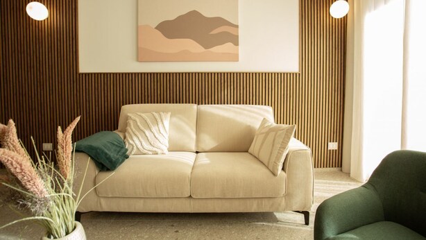 A living room with a beige sofa, a green armchair, and a wall-mounted painting of a landscape. - Palazzo Indaco - RESIDENZA SMERALDO (Castel di Sangro)