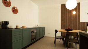 A compact kitchen with green cabinets, a built-in oven, and a dining area with a wooden table and chairs. - Palazzo Indaco - RESIDENZA SMERALDO (Castel di Sangro)