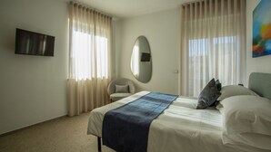A hotel room with a bed, a chair, a TV, and a large window with curtains. - Palazzo Indaco - RESIDENZA SMERALDO (Castel di Sangro)