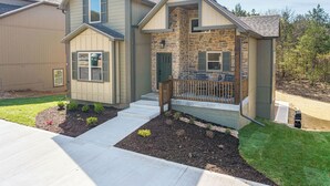 A two-story house with a stone facade, a front porch with a railing, and a small front yard with mulch and plants. - HUGE Private Heated Swim Spa • Game Room • 7BR/7BA • Entire home • Work Space (Hollister)