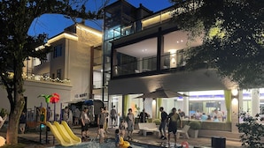 A swimming pool area with a slide, surrounded by a building with a glass facade and outdoor seating. - Lin an Hot Spring Story Family Homestay (Hangzhou)