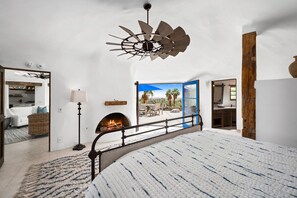 Un dormitorio con una cama grande, chimenea, ventilador de techo y vistas al exterior.