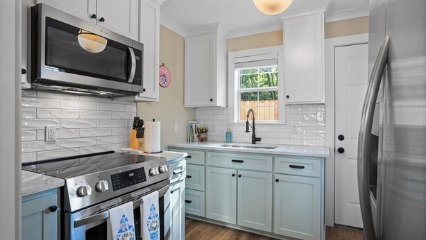 A modern kitchen with white cabinets, stainless steel appliances, and a window with a view of greenery. - Cottage Row: Daphne (Laurel)