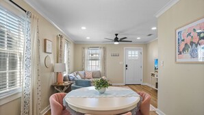 A dining area with a round table and pink chairs, a ceiling fan, and a door in the background. - Cottage Row: Daphne (Laurel)