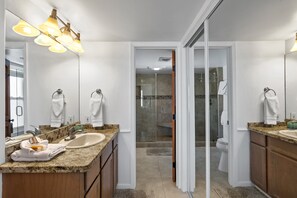 A modern bathroom with a large mirror, granite countertops, a sink, and a shower area.