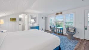 Ein Schlafzimmer mit einem großen Bett, einem Schminktisch, einem Schrank, einem Sessel und einem Fenster mit Jalousien.