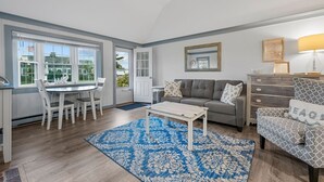 A living room with a dining area, a gray sofa, a coffee table, and a blue patterned rug. - Seaside Charm Awaits at The Duckling (South Yarmouth)