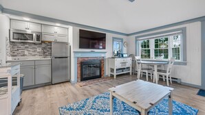 A modern kitchen with a built-in microwave, refrigerator, and a fireplace. There is a dining area with a table and chairs. - Seaside Charm Awaits at The Duckling (South Yarmouth)
