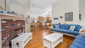 A living room with a fireplace, a sofa, and a dining area with wooden cabinets. - Roomy 3 Bedroom Home - Perfect for Families! (Dennis)