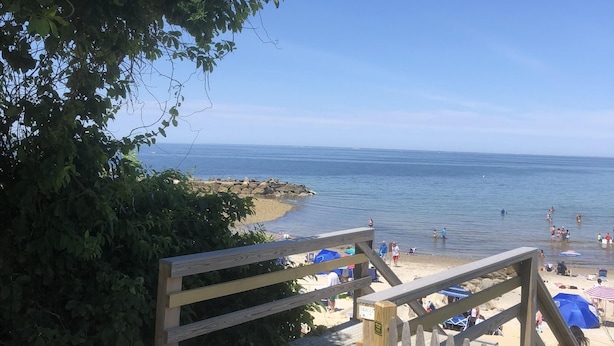 A wooden staircase leading to a beach with umbrellas and people in the water. - Roomy 3 Bedroom Home - Perfect for Families! (Dennis)