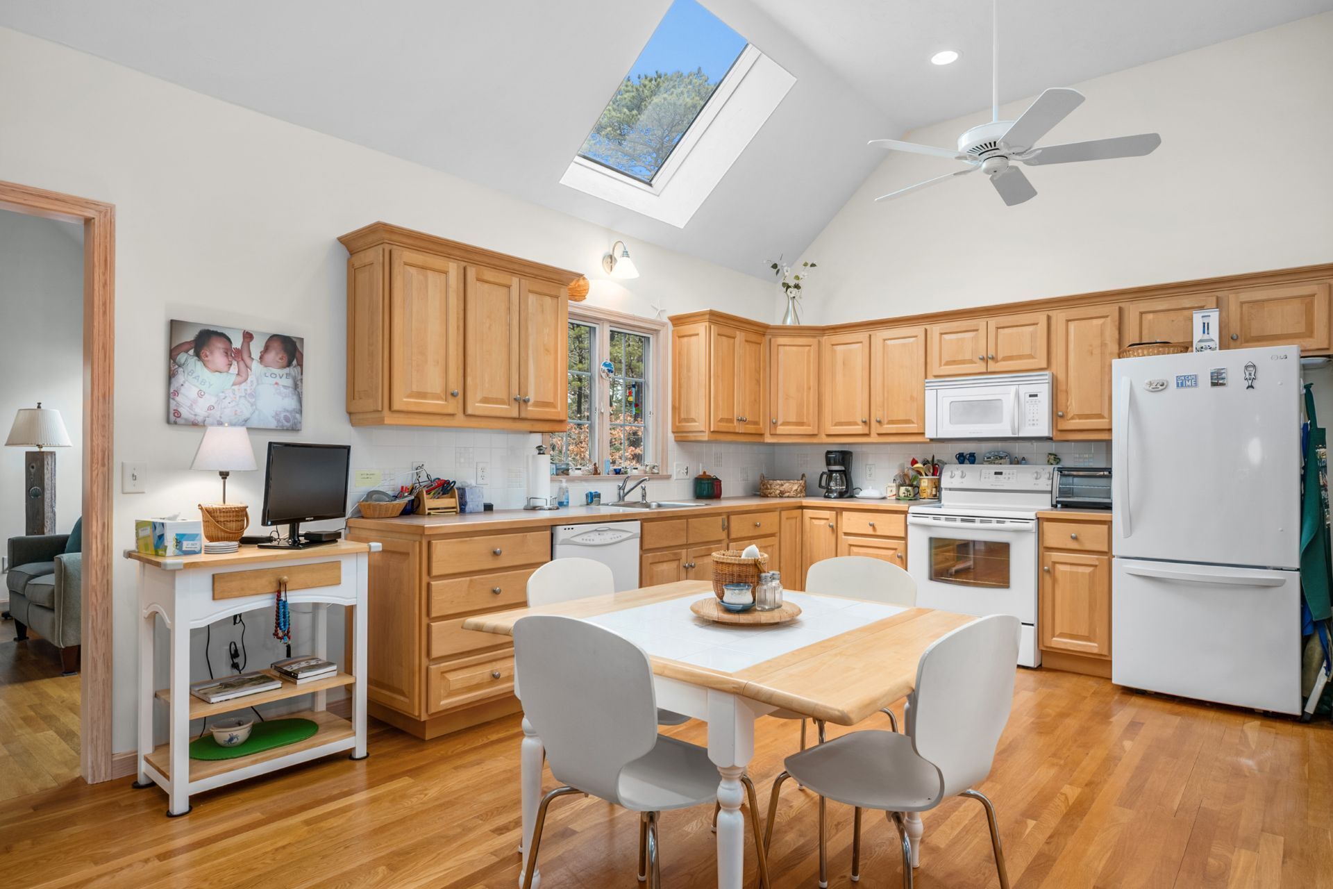 A modern kitchen with wooden cabinets, a dining table with chairs, a ceiling fan, and a skylight.