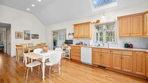 A spacious kitchen with wooden cabinets, a dining area with white chairs, and a large window providing natural light. - Roomy 3 Bedroom Home - Perfect for Families! (Dennis)