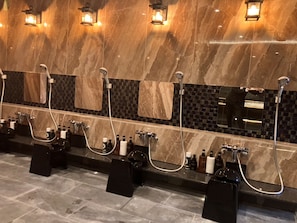 A public restroom with multiple sinks, each equipped with a handheld showerhead, and a tiled wall with a mosaic pattern. - HOTEL LiVEMAX Tendo (Tendo)