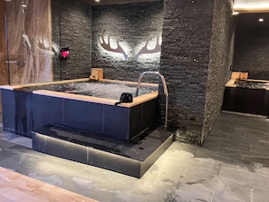 A spa area with a hot tub, a wooden bench, and a stone wall with a deer silhouette. - HOTEL LiVEMAX Tendo (Tendo)
