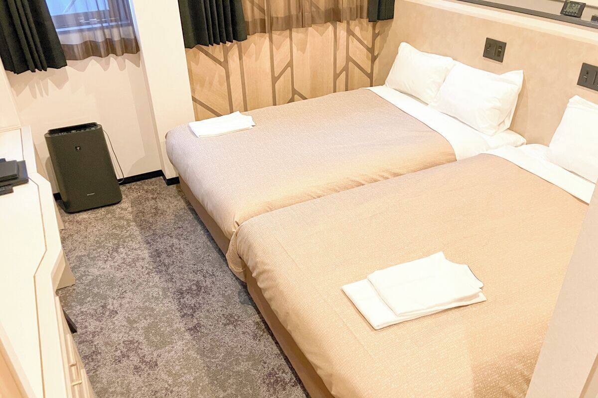 A hotel room with two beds, a small desk, and a speaker.