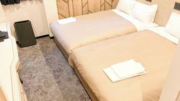 A hotel room with two beds, a small desk, and a speaker.