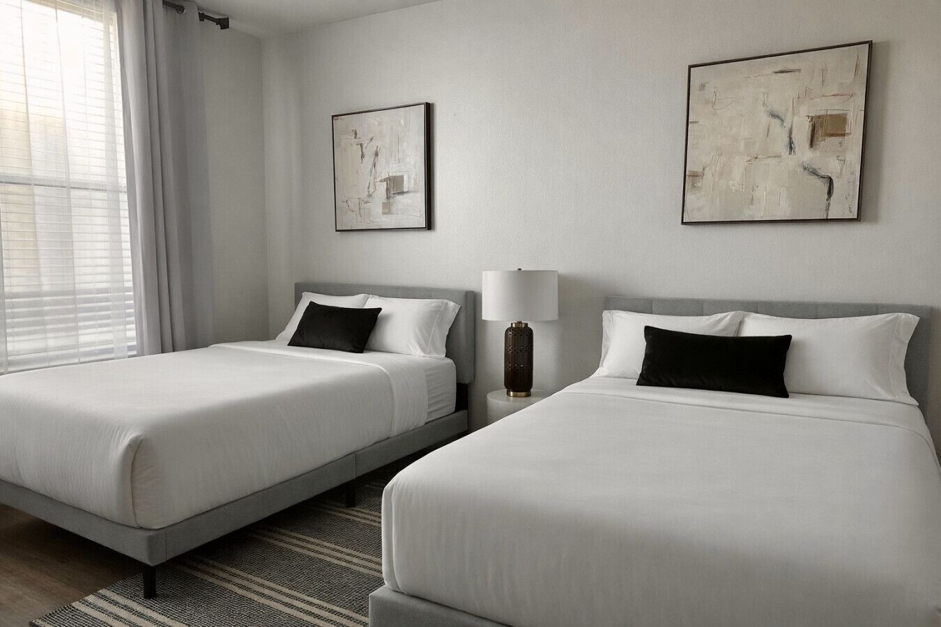 Una camera d'albergo con due letti, un comodino con lampada e due dipinti astratti alle pareti.