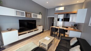 A modern living room with a flat-screen TV, a sofa, a coffee table, and a dining area with a kitchen in the background. - Apartment center Carmes (Toulouse)