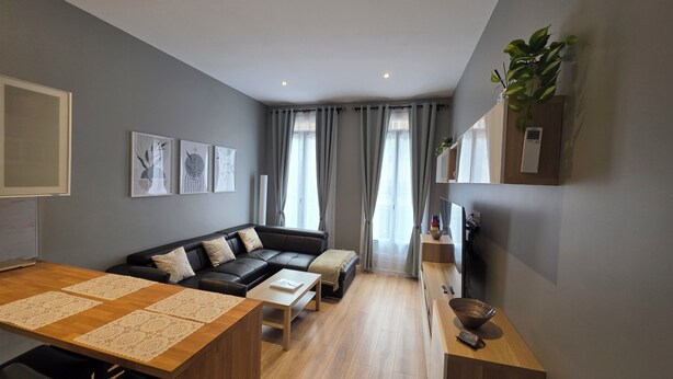 A modern living room with a wooden dining table, a black leather sofa, and a small coffee table. - Apartment center Carmes (Toulouse)