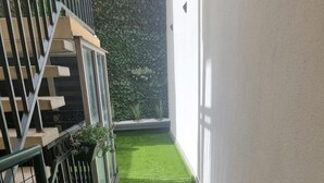 A narrow corridor with artificial green turf and stepping stones, bordered by a metal railing and a white wall. - Apartment center Carmes (Toulouse)