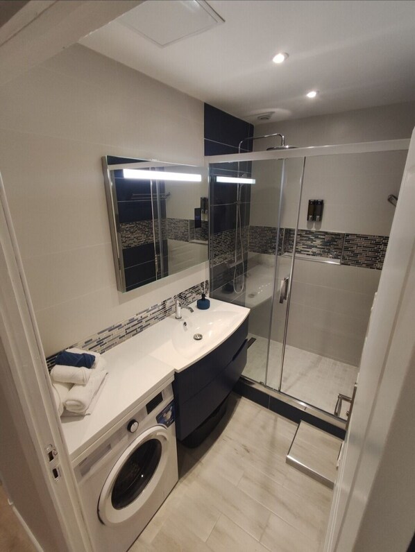 Une salle de bain moderne dotée d’une douche à parois de verre, d’un lave-linge encastré et d’un grand miroir au-dessus du lavabo.