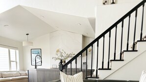 Ein modernes Wohnzimmer mit einem schwarzen Ledersofa, einem weißen Hocker und Holzdielen.
