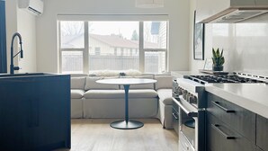 Eine moderne Küche mit Backofen, ein Essbereich mit rundem Tisch und Blick auf eine Wohngegend durch große Fenster.