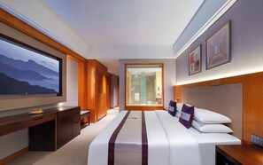 Une chambre d’hôtel avec un grand lit, un bureau, une télévision et une salle de bain visible à travers une porte en verre.