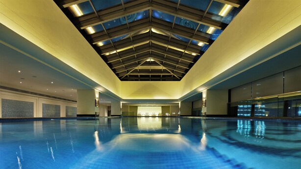 Une grande piscine intérieure dotée d’un haut plafond et de fenêtres de toit.