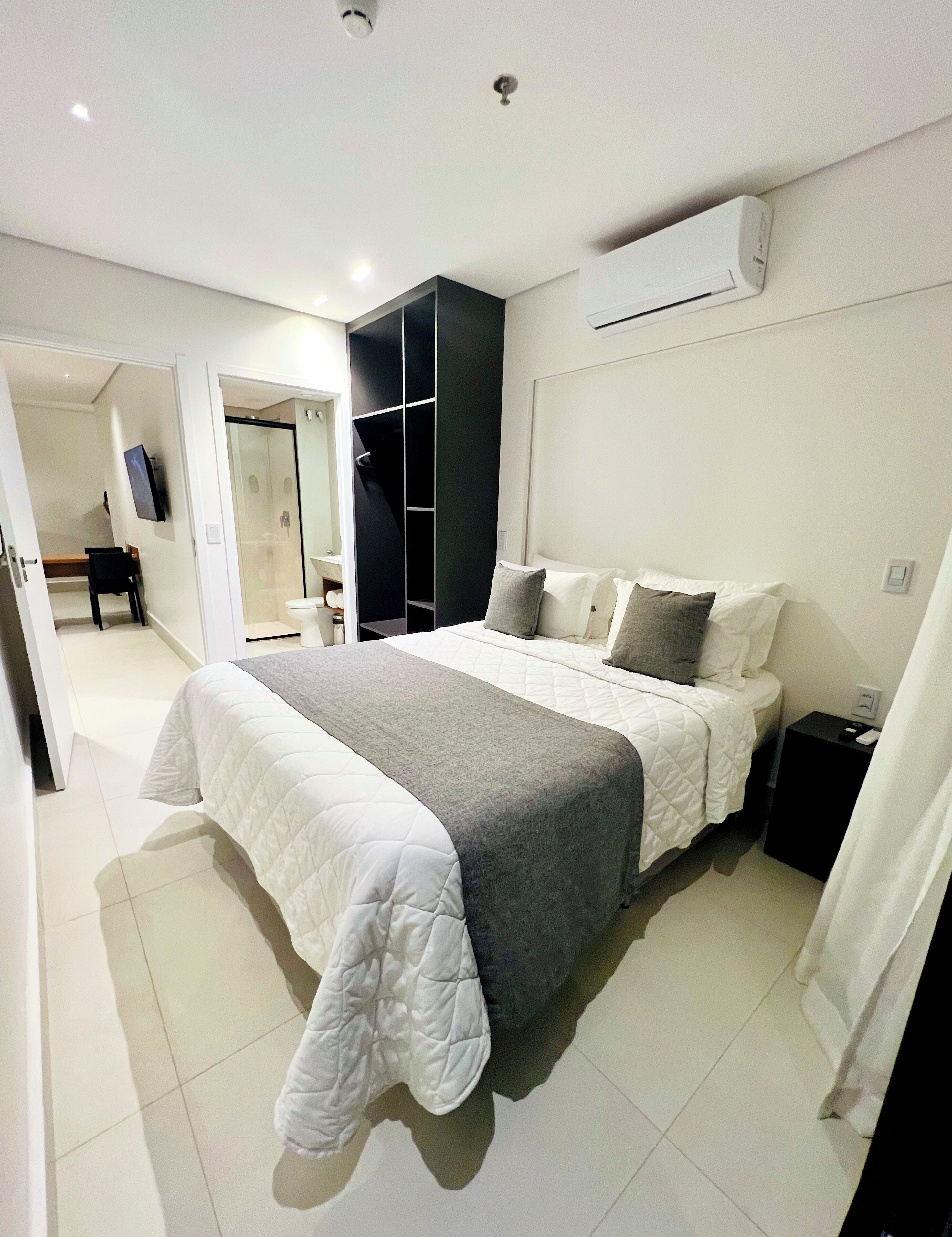 Un dormitorio moderno con una cama grande, un vestidor y un baño visible a través de una puerta abierta.