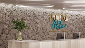 A reception desk with a stone wall backdrop, a potted plant, and a sign reading "PORTO Alito". - Porto Alto Resort - Pé na Areia (Ipojuca)