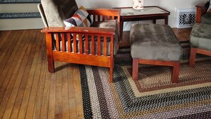Una sala de estar con piso de madera, un sofá, una mesa de centro y una lámpara. Se observa una escalera al fondo.