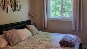 A bedroom with a bed, a window with curtains, a wall-mounted light fixture, and geometric wall art.