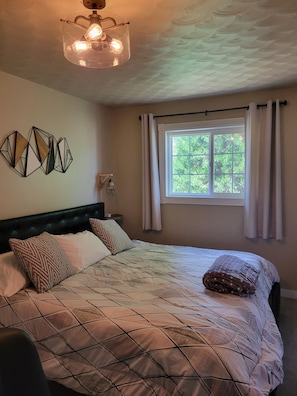 Une chambre à coucher avec un lit, une fen être avec des rideaux, un luminaire fixé au mur et des œuvres d’art géométriques sur le mur.