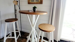 A kitchen with two white stools, a wooden table, and a vintage coffee sign.