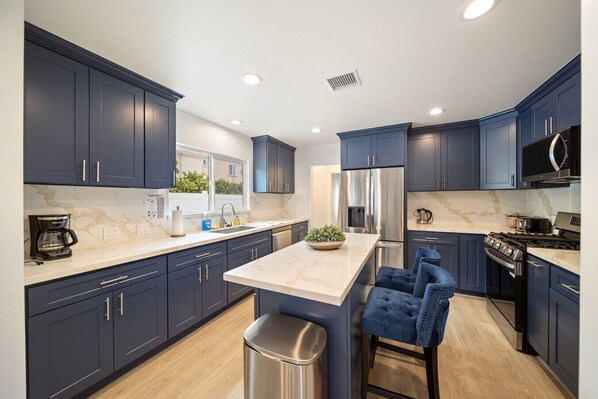 A modern kitchen with dark blue cabinets, stainless steel appliances, and a marble countertop.