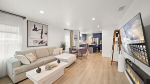 A modern living room with a sofa, coffee table, and fireplace. There is a kitchen in the background with a dining area.